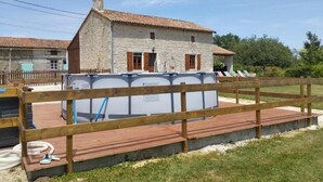 Una casa de pedra amb teulada a falça, una zona de piscina tancada i un pont d'obra.
