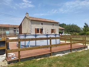 Ein Steinhaus mit einem Ziegeldach, einem eingezäunten Poolbereich und einer Holzterrasse.