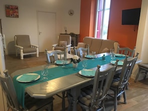 Un espace repas avec une longue table dressée pour quatre personnes, entourée de chaises en bois.