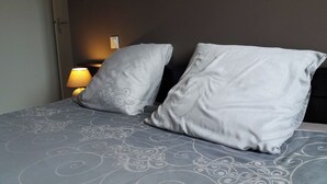 A bed with a patterned bedspread and two pillows, a bedside lamp, and a wall-mounted light fixture. - Le Grand Gîte - LATHUS-SAINT-REMY (LATHUS-SAINT-REMY)