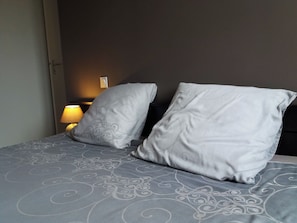 Un lit avec une couvre-lit à motifs et deux oreillers, une lampe de chevet et un luminaire fixé au mur.