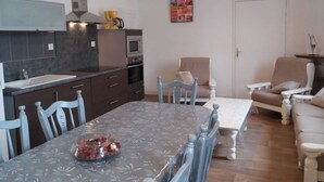 A compact kitchen with a dining area, a sofa, and a table with a bowl of fruit. - Le Grand Gîte - LATHUS-SAINT-REMY (LATHUS-SAINT-REMY)