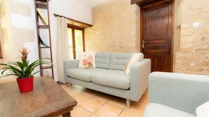 A room with a light-colored sofa, a wooden table with a red pot, a ladder, and a stone wall. - Gite de la Poupardière (CLOUE)