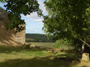 A stone building with a picnic table and a bench, surrounded by greenery and a view of a lake. - Gite de la Poupardière (CLOUE)