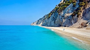 A coastal beach with clear turquoise waters and rocky cliffs.