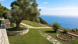 A landscaped garden with a stone pathway, a large tree, and a view of the sea. - Anerada Houses - Seaviews Above Egremni in Lefkada (Lefkada)