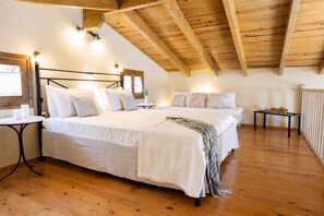 A bedroom with a wooden ceiling, a bed with white bedding, a small table, and a window.