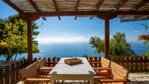 A covered outdoor seating area with a table and chairs, overlooking a scenic view of the sea. - Anerada Houses - Seaviews Above Egremni in Lefkada (Lefkada)