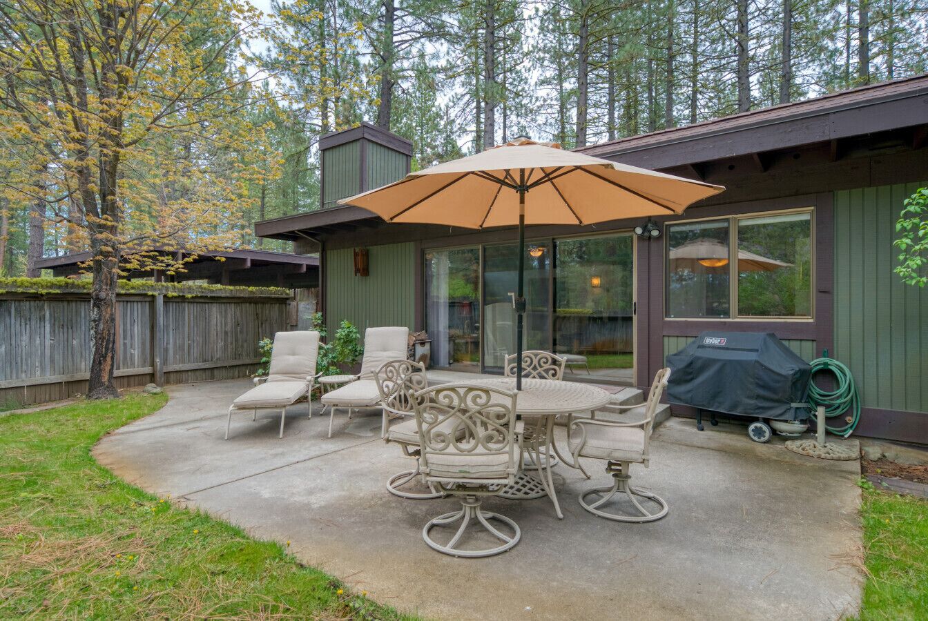 An outdoor patio with a table and chairs, a covered umbrella, and a barbecue grill.