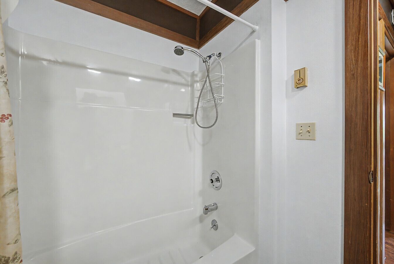 A bathroom with a bathtub, shower, and a wooden ceiling beam.