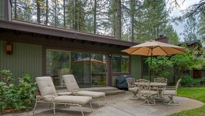 Un patio couvert, doté de chaises longues et d’une table, entouré d’une terrasse en bois et offrant une vue sur les arbres.