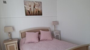 Une chambre à coucher comprenant un lit, deux tables de chevet, une lampe fixée au mur, une armoire et une œuvre d’art à motifs floraux.