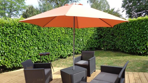 Un espace extérieur aménagé en terrasse, avec des meubles en osier, une table et un grand parasol.