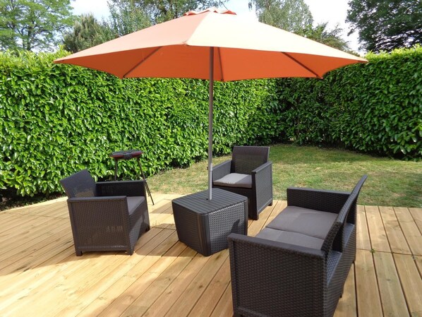 An outdoor patio area with wicker furniture, a table, and a large umbrella. - Les 3 Nichoirs - LIGUGE (LIGUGE)