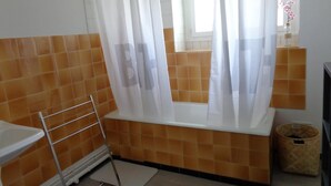 Une salle de bain avec une baignoire, un rideau de douche, une fenêtre et un mur carrelé.