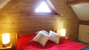 A bedroom with a red bedspread, two pillows, a wooden headboard, a nightstand with a lamp, and a triangular skylight. - Asia - BUSSIERE (LA) (BUSSIERE (LA))
