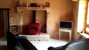 Een landelijke kamer met een stenen openhaard, een rode houtkachel, een televisie op een standaard en leren banken.