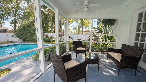 Eine überdachte Terrasse mit Korbmöbeln, einem Deckenventilator und Blick auf einen Swimmingpool.