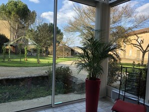 A room with a large glass window, a red potted plant, and a metal chair. - La Malinerie - ASLONNES (ASLONNES)