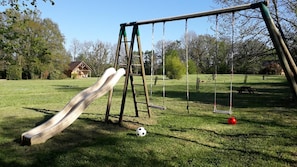 A playground with a slide, swings, and a soccer ball on the grass.