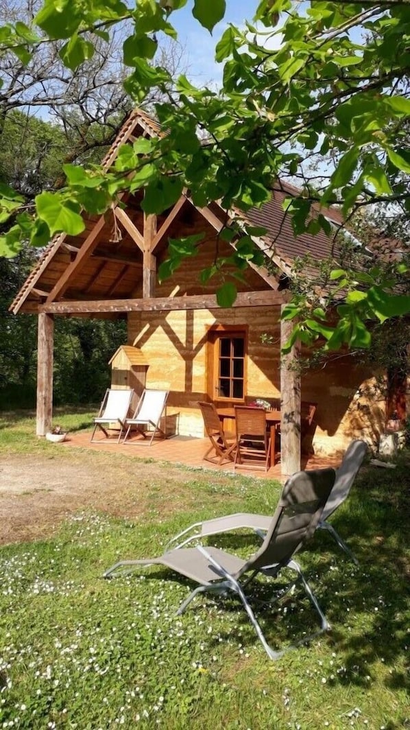 A wooden cabin with a covered porch, two lounge chairs, and a dining table.