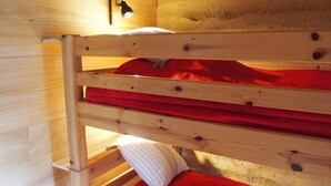 A bunk bed with a red blanket and pillow, wooden walls, and a wall-mounted light fixture.