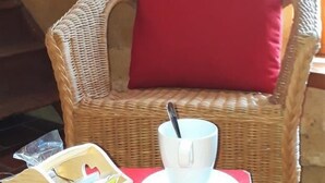 A wicker chair with a red cushion, a white cup with a spoon, and a cardboard box on a red table.