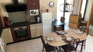 A kitchen with a dining table set for four, a microwave, a refrigerator, and a stove. - Le Relais de la Motte (THURE)