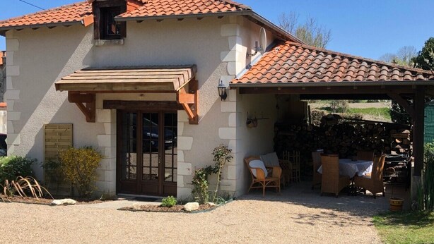 A house with a tiled roof, a front door, and a covered patio area with outdoor furniture. - Le Relais de la Motte (THURE)
