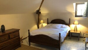 A bedroom with a wooden bed, a dresser, two bedside lamps, and a window with curtains. - Le Relais de la Motte (THURE)