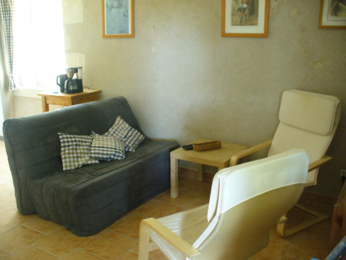 A living room with a dark grey sofa, a white armchair, a small wooden table, and a coffee maker on a side table.