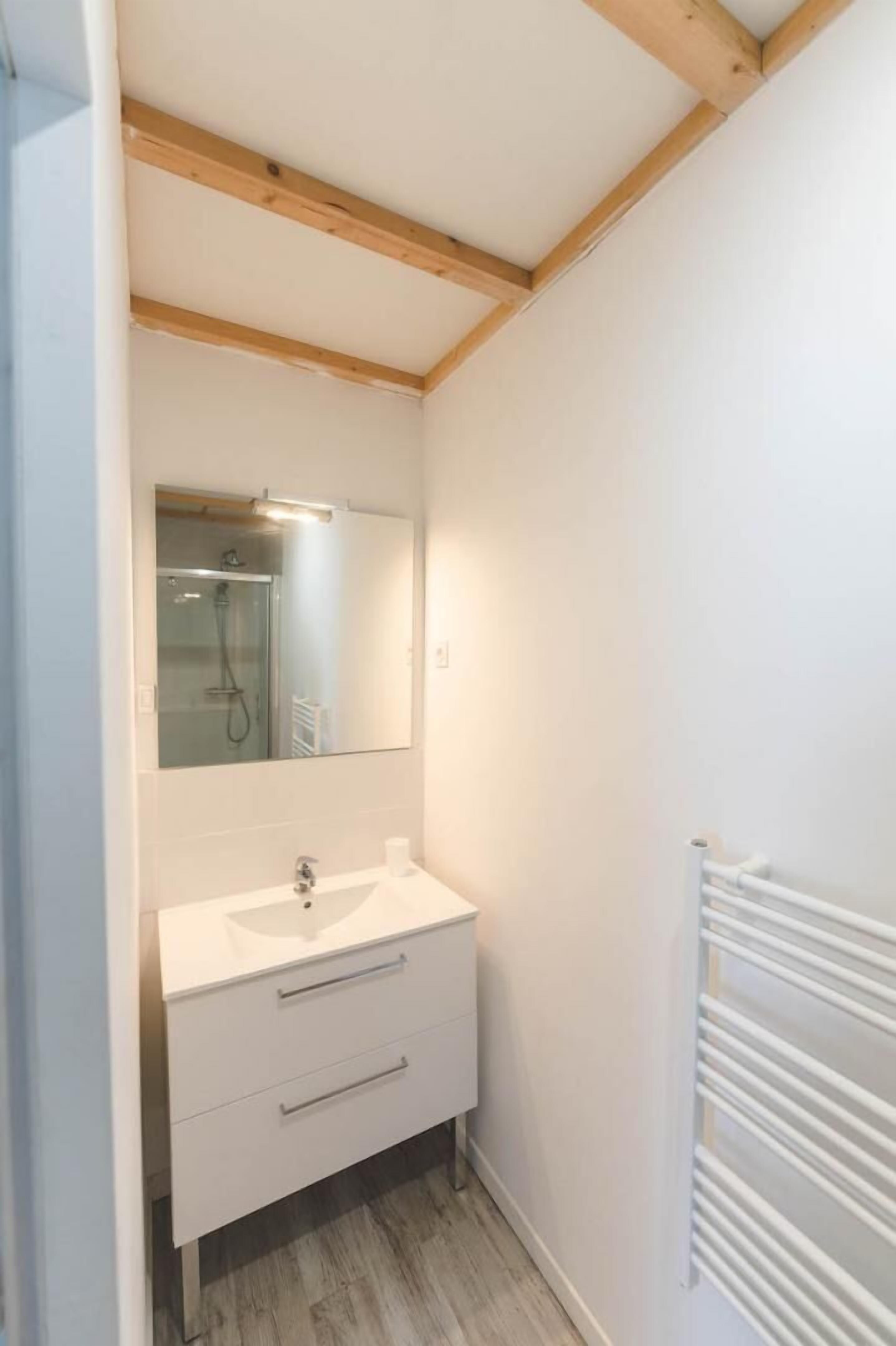 Een compacte, moderne badkamer met een witte wastafel, spiegel en houten balken in het plafond.