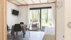 Habitació amb sostre de fusta, un llit, una televisió, una taula amb cadires i una porta corredissa de vidre que dona a una zona exterior.