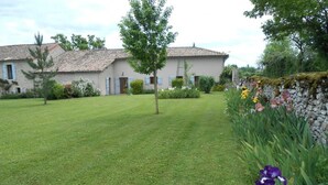 Une maison avec un toit en tuiles, une pelouse bien entretenue et un mur de pierres orné de fleurs.