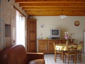 Ein Wohnzimmer mit braunem Ledersofa, einem Holzesstisch mit Stühlen, einem Fernseher und einer Holzkommode.