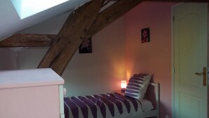 Ein kleines Schlafzimmer mit schrägem Dach, einem Einzelbett, einem Nachttisch mit Lampe und einer Tür.