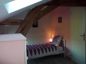 A small bedroom with a sloped ceiling, a single bed, a nightstand with a lamp, and a door. - Le Gîte de L'Esservier (PERSAC)