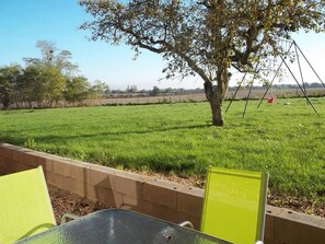 A table with chairs in a grassy outdoor area with a tree and a swing set in the background. - Le Gîte de L'Esservier (PERSAC)