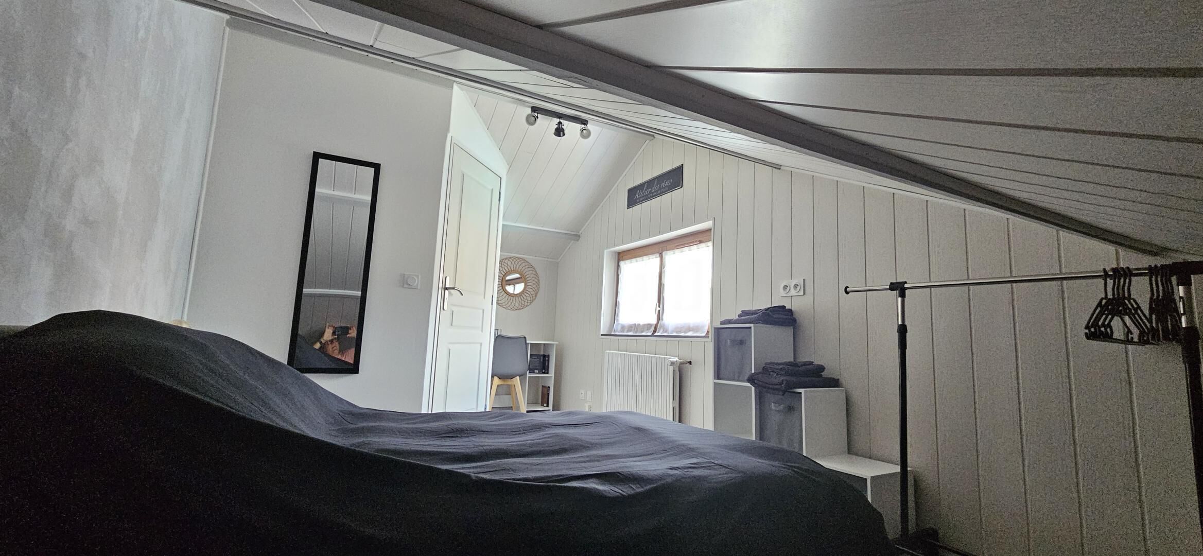 A bedroom with a bed, a wardrobe, a mirror, a window, and a door leading to another room.