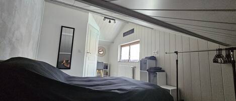 A bedroom with a bed, a wardrobe, a mirror, a window, and a door leading to another room.