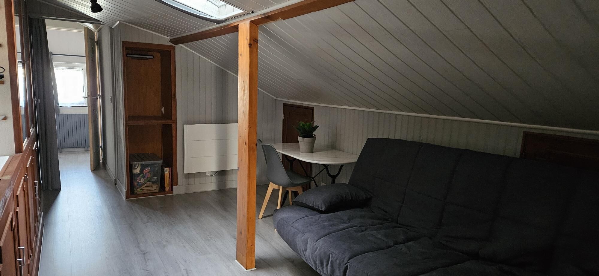 A loft-style room with a high ceiling, a built-in desk with a chair, a sofa, and a small potted plant.