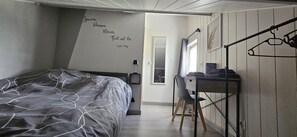 Ein Schlafzimmer mit Bett, Schreibtisch, Stuhl, Fenster und einer Wand mit einem Zitat.