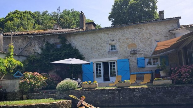 Ein Steinhaus mit einem Fluss davor, einem Kajak und Außenplätzen.