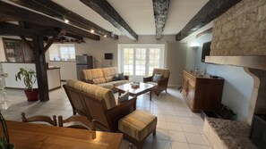 A spacious living area with a sofa, chairs, a wooden table, a kitchen area, and a stone fireplace. - Au bord du Clain - ROMAGNE (ROMAGNE)