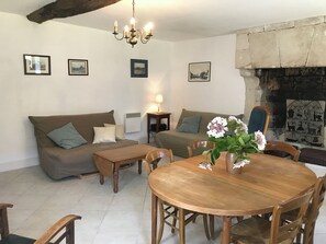 A living room with a sofa, a dining table with chairs, a chandelier, and a fireplace. - Gîte Lamarlière - SAVIGNY-SOUS-FAYE (SAVIGNY-SOUS-FAYE)