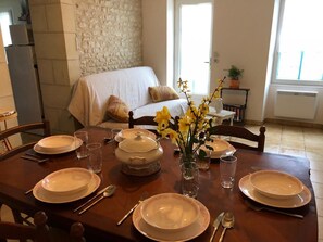 A dining table set with plates, glasses, cutlery, and a centerpiece of yellow flowers. - La Petite Maison Bleue (SOSSAIS)