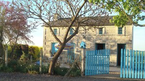 Ein Steinhaus mit blauem Tor und einem Baum davor.