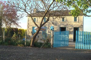 Ein Steinhaus mit blauem Tor und einem Baum davor.