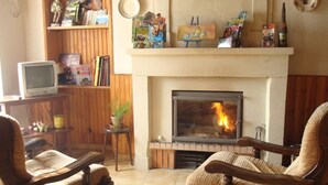 Ein Wohnzimmer mit Kamin, zwei Holzstühlen, einem Fernseher und einem Bücherregal mit verschiedenen Gegenständen.