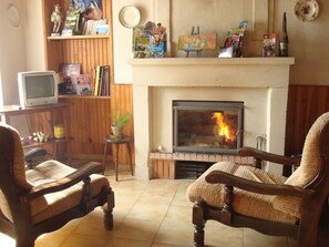 Ein Wohnzimmer mit Kamin, zwei Holzstühlen, einem Fernseher und einem Bücherregal mit verschiedenen Gegenständen.